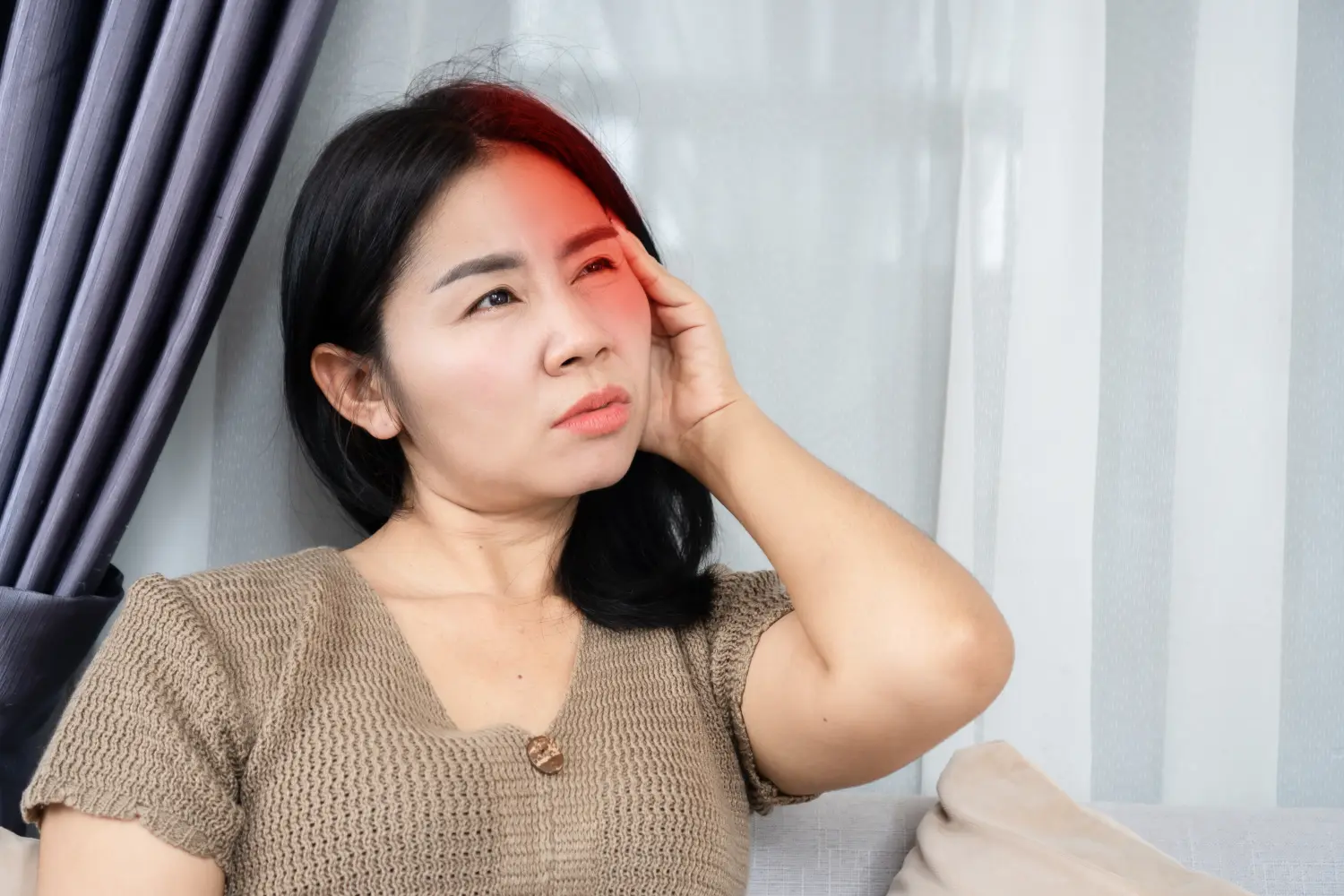 Asiatische Frau leidet unter Migränekopfschmerzen und verspürt Schmerzen auf einer Seite ihres Kopfes
